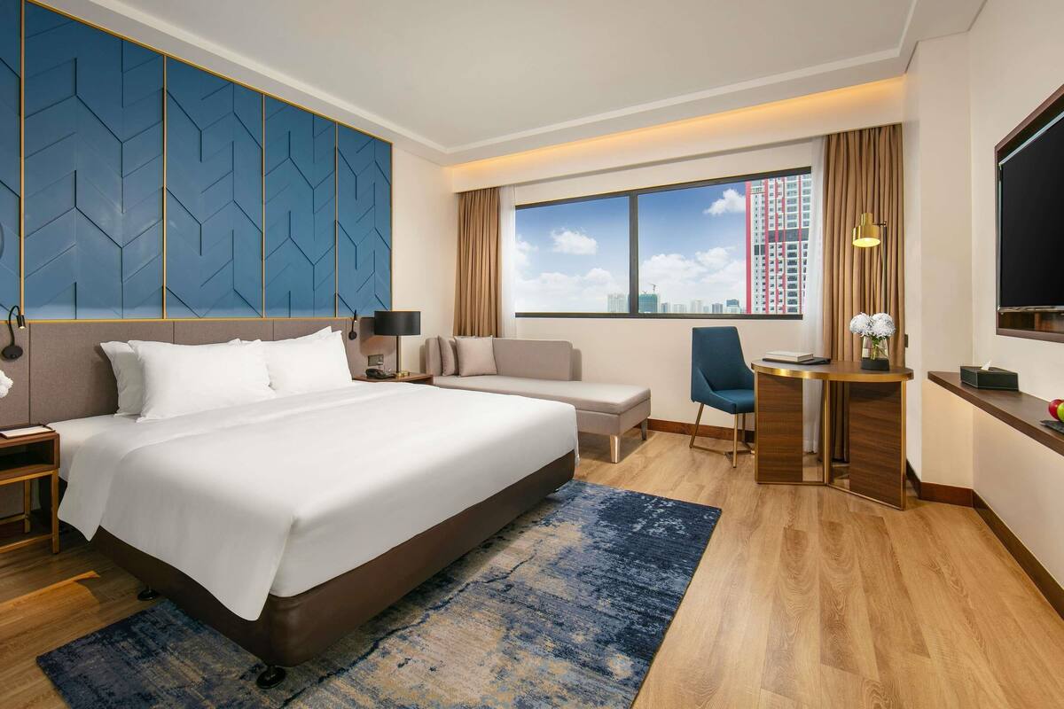Habitación de hotel con una cama grande, un escritorio, una silla y vistas a la ciudad.