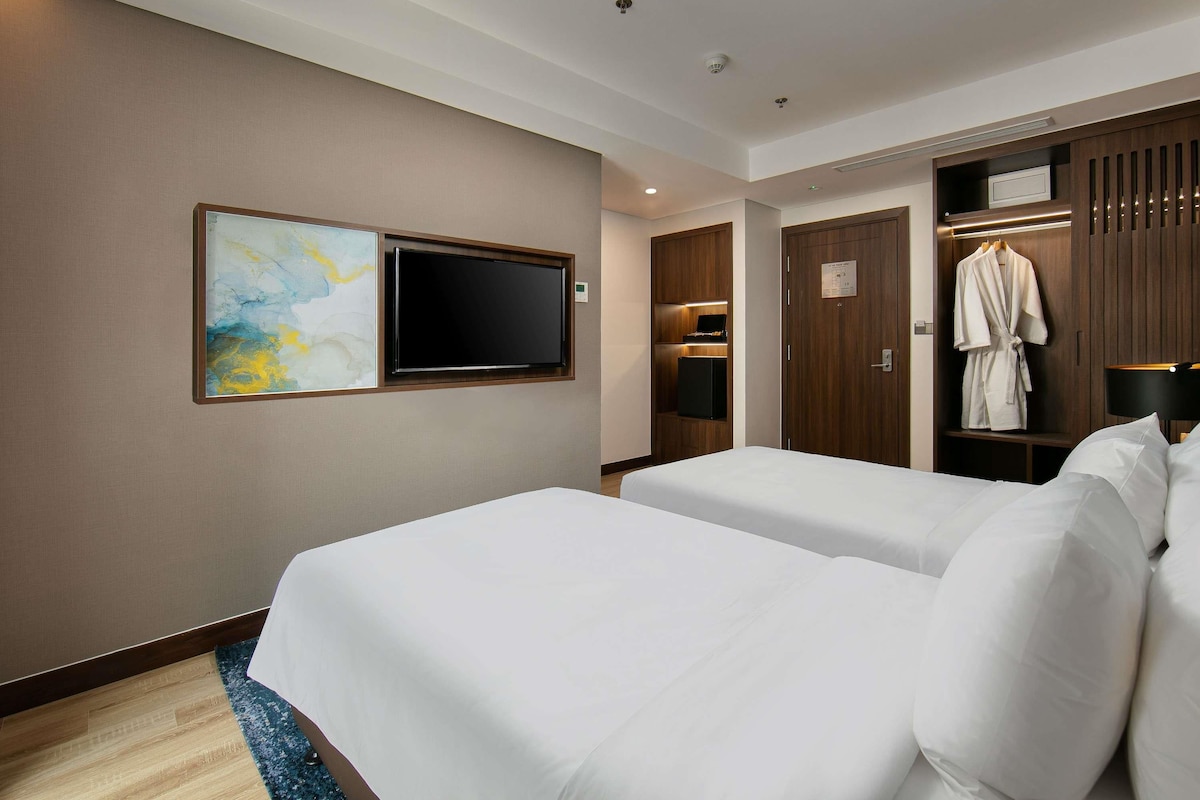 Hotelkamer met twee bedden, een flatscreen televisie, een badjas hangend aan een deur en een schilderij aan de muur.