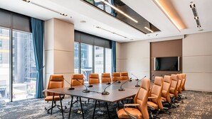 A conference room with a long table, multiple chairs, microphones, and a large screen.