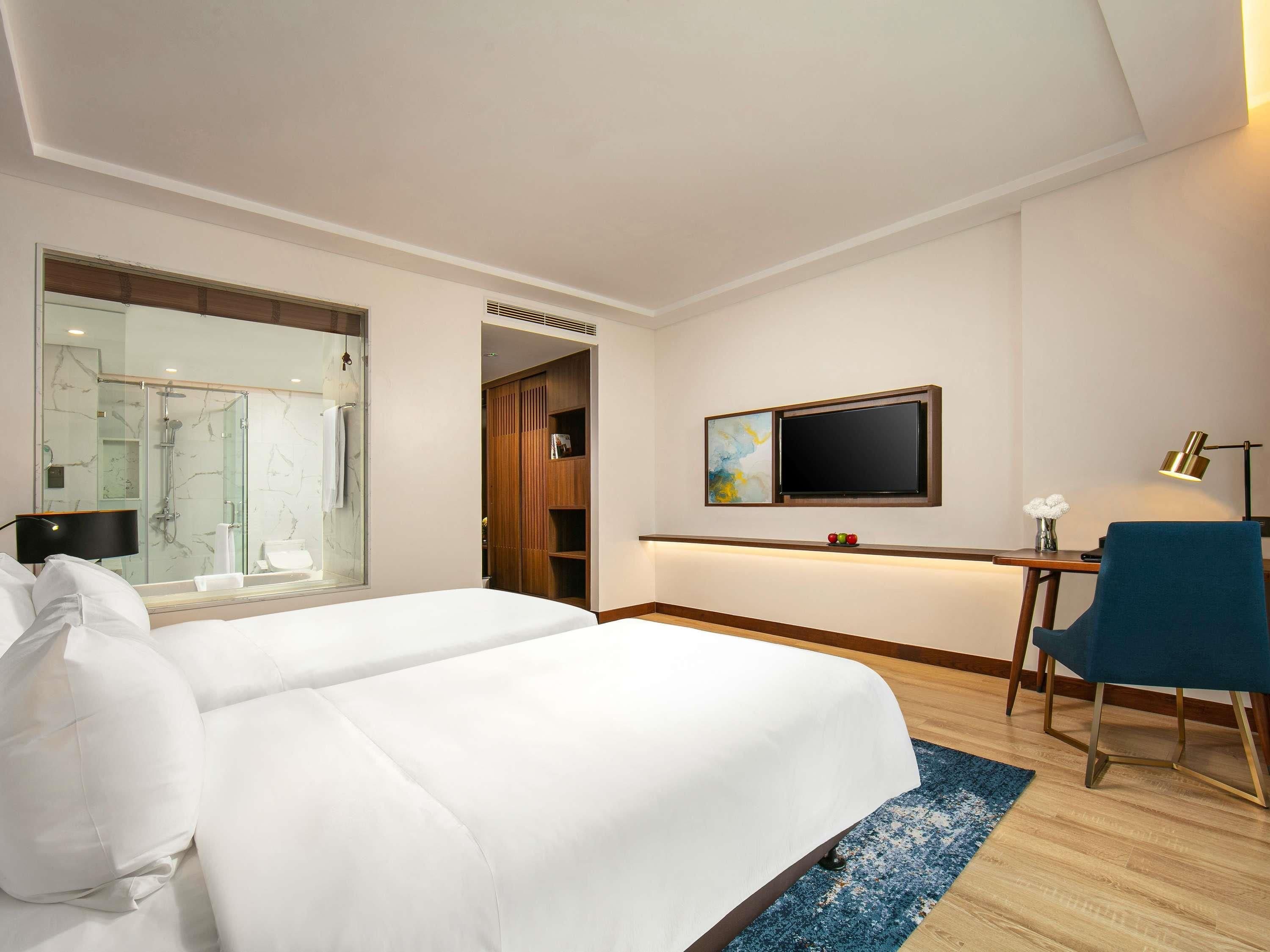 Habitación de hotel con una cama grande, un escritorio con silla, televisión y zona de ducha.