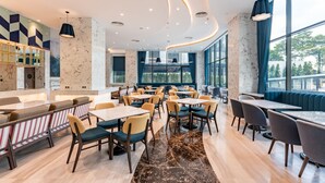 Un restaurante moderno con paredes de mármol, ventanas amplias y diversas opciones de asientos, como mesas y cabinas.