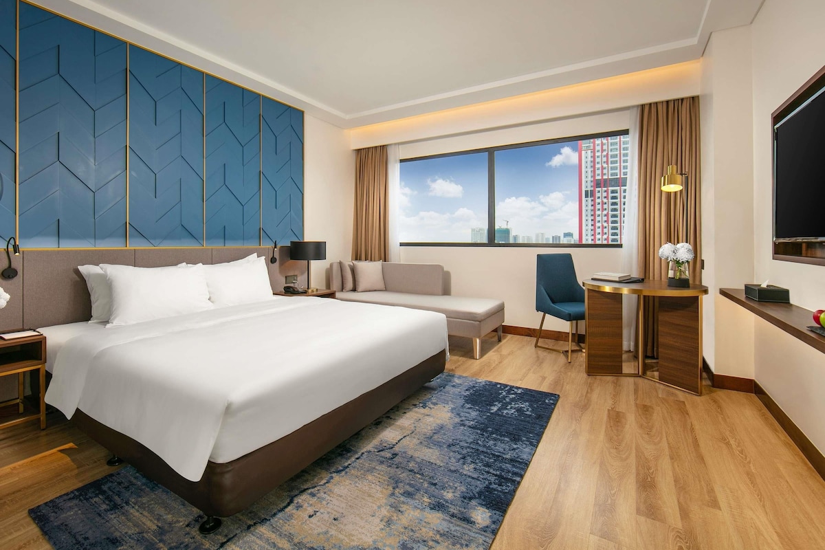 Een hotelkamer met een groot bed, een bureau, een stoel en uitzicht op de stad.