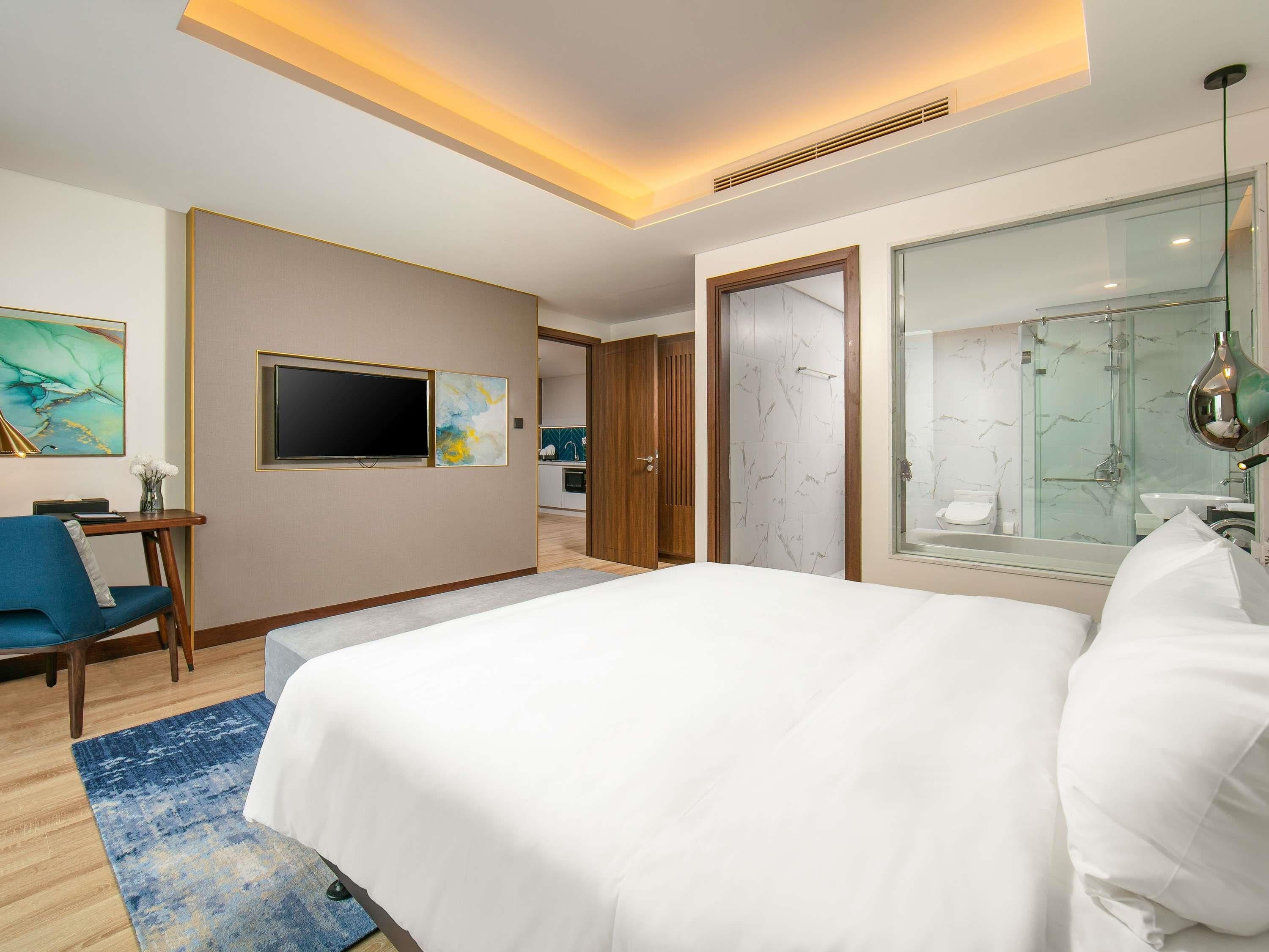 Hotelkamer met een bed, een bureau, een stoel, een televisie, een badkamer met douche en een schilderij aan de muur.