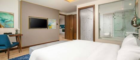 Hotelkamer met een bed, een bureau, een stoel, een televisie, een badkamer met douche en een schilderij aan de muur.