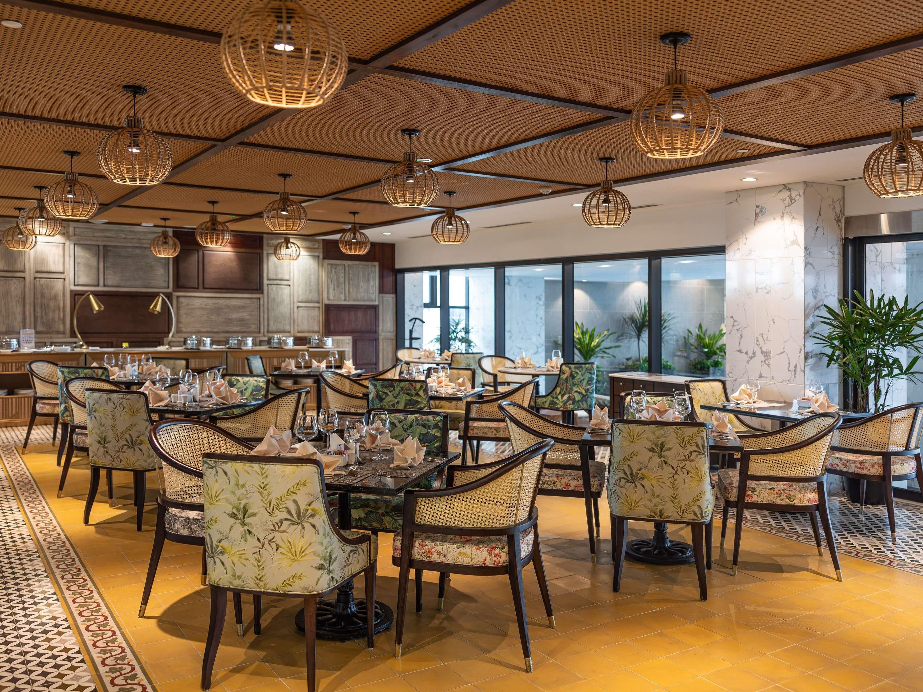 Un restaurante con mesas redondas, sillas de mimbre e iluminación colgante.