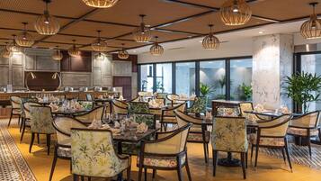 Un restaurante con mesas redondas, sillas de mimbre e iluminación colgante.