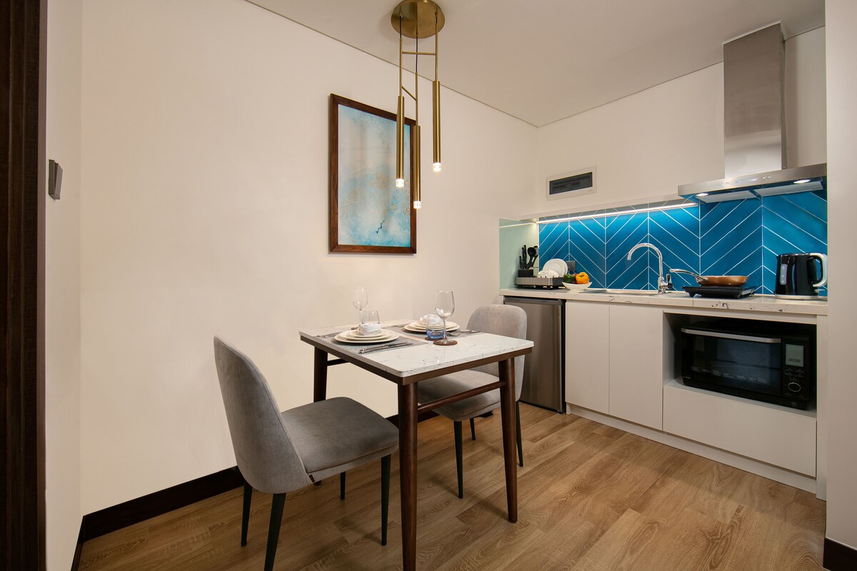 Une cuisine moderne avec un coin repas, dotée d’un plan de travail blanc, d’un pare-feu bleu et d’un luminaire suspendu.