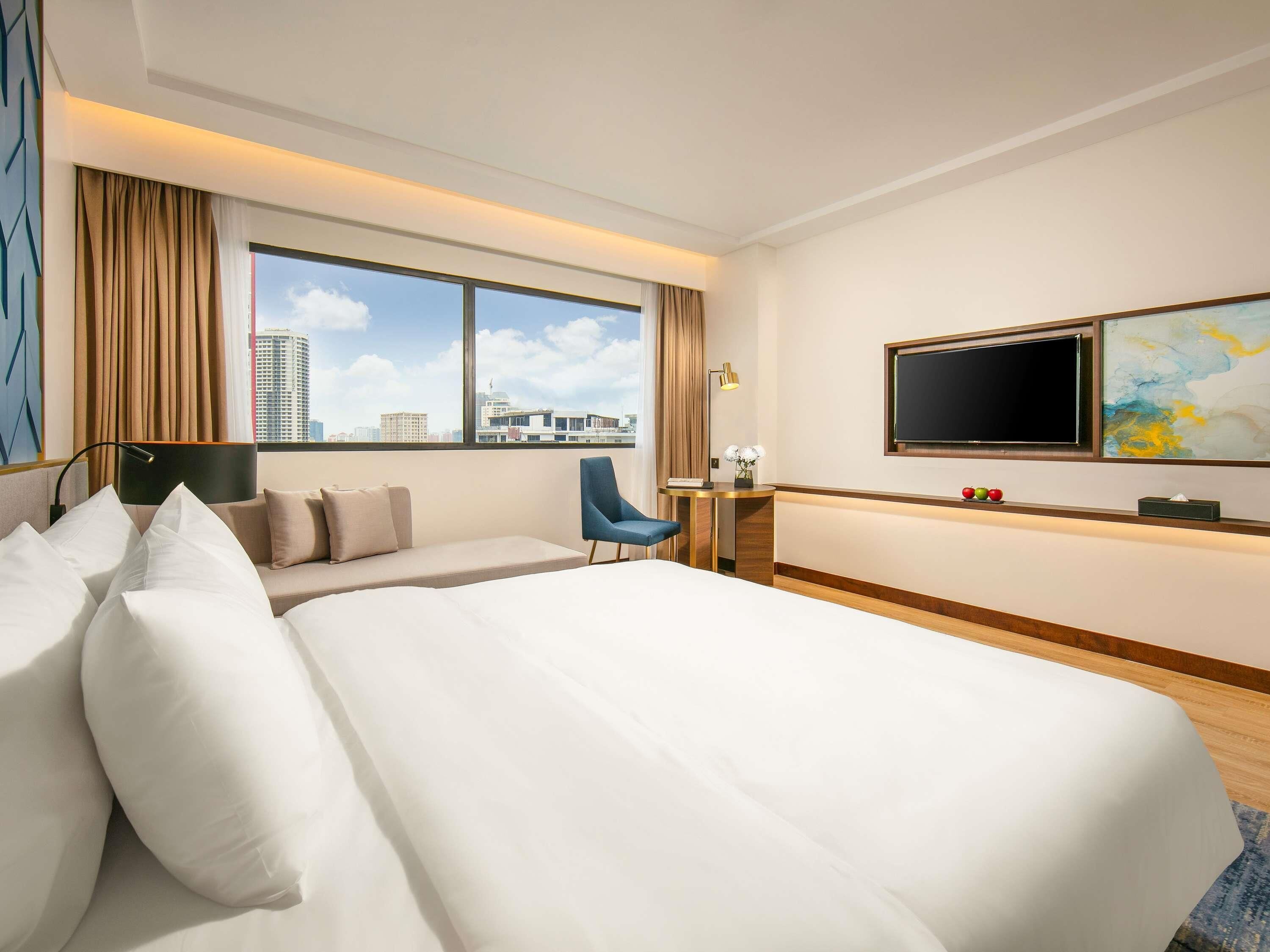 Una camera d'albergo con un letto grande, una scrivania, una sedia, una TV e vista sulla città.
