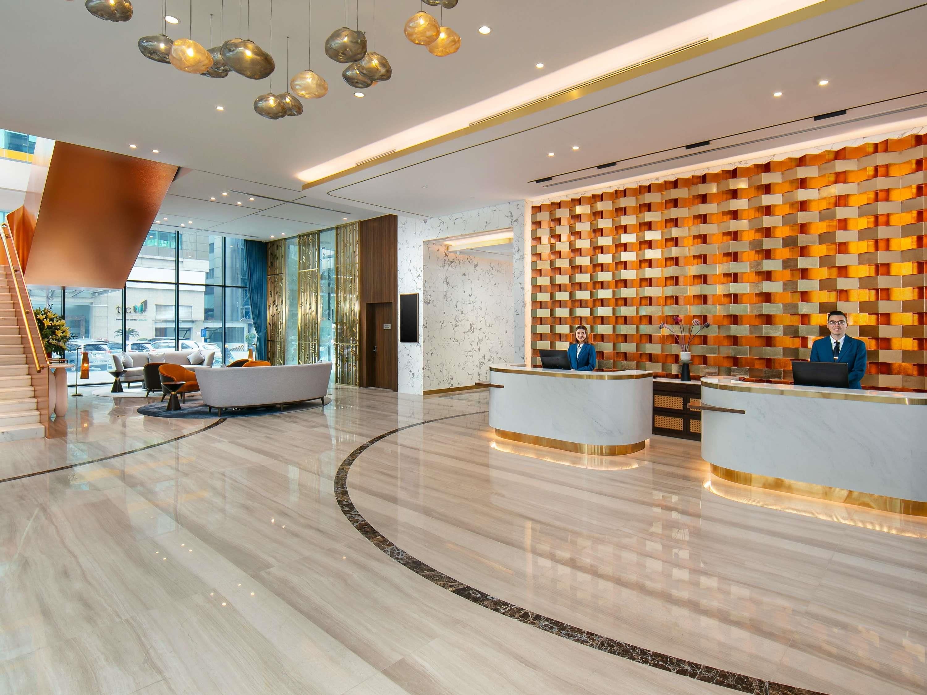 A modern hotel lobby with a reception desk, seating area, and a staircase.