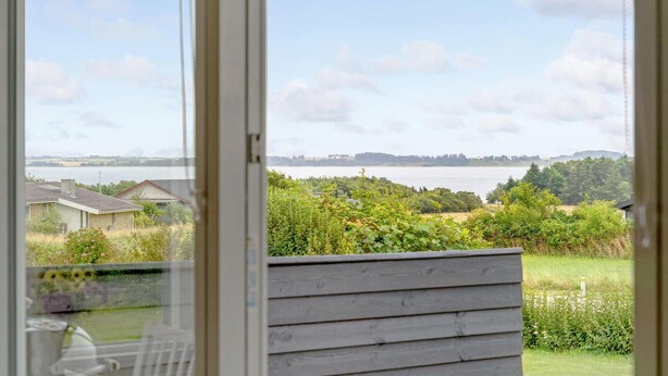 En utsikt från ett fönster med utsikt över en sjö, med en träveranda och en gräsyta i förgrunden.