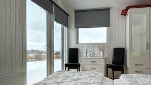 Ett sovrum med ett stort fönster, två stolar, en byrå och en spegel.