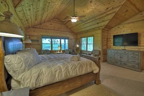 Ein Schlafzimmer in einer Blockhütte mit einem Bett, einem Deckenventilator, einem Fernseher und einer Kommode.