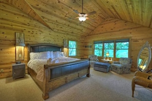 Ein Schlafzimmer einer Holzhütte mit einem Bett, zwei Stühlen, einem kleinen Tisch und einem Deckenventilator.