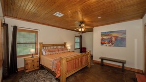 Une chambre avec un plafond en bois, un lit avec une literie à motifs, un banc et un tableau accroché au mur.