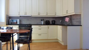 Una cocina con armarios blancos, encimera negra, microondas, horno y zona de comedor con mesa y sillas.