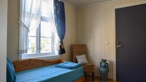 Una habitación con una cama de madera, una silla de mimbre, un jarrón azul y una puerta.