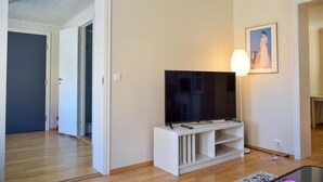 Una sala de estar con un televisor de pantalla plana sobre un mueble blanco, un cuadro en la pared y una lámpara.