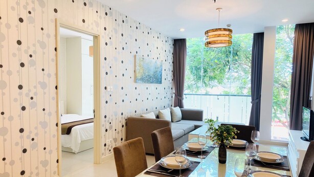 Uma sala de jantar moderna com uma mesa de vidro posta para quatro pessoas, um sofá e um quadro na parede.