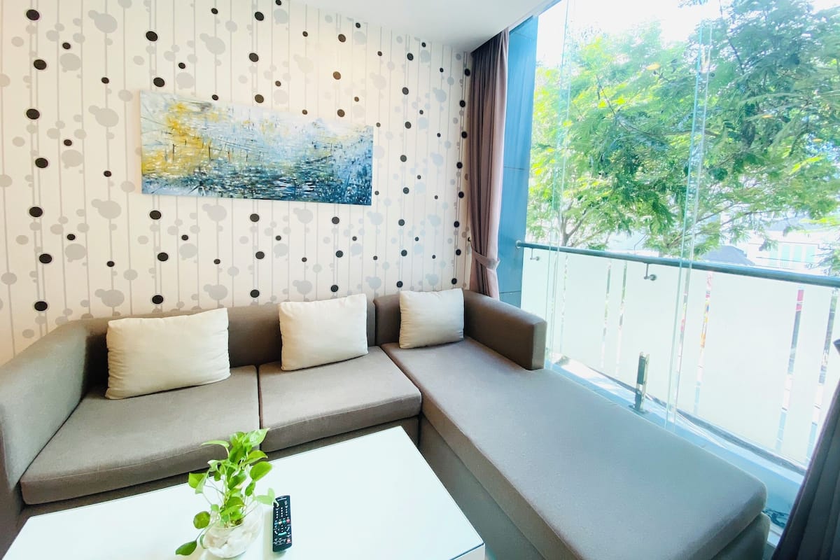 Ein modernes Wohnzimmer mit einer Eckcouch, einem Couchtisch und einem großen Fenster mit Blick auf Bäume.