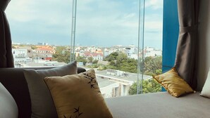 Quarto com uma grande janela, um sofá com almofadas e vista para a paisagem urbana.