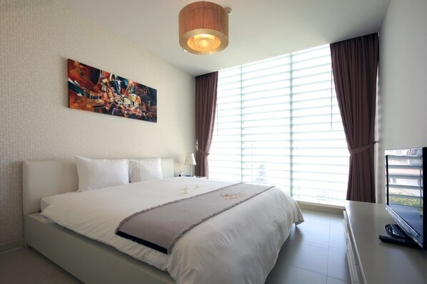 A hotel room with a large bed, a painting on the wall, a window with curtains, and a television on a stand.