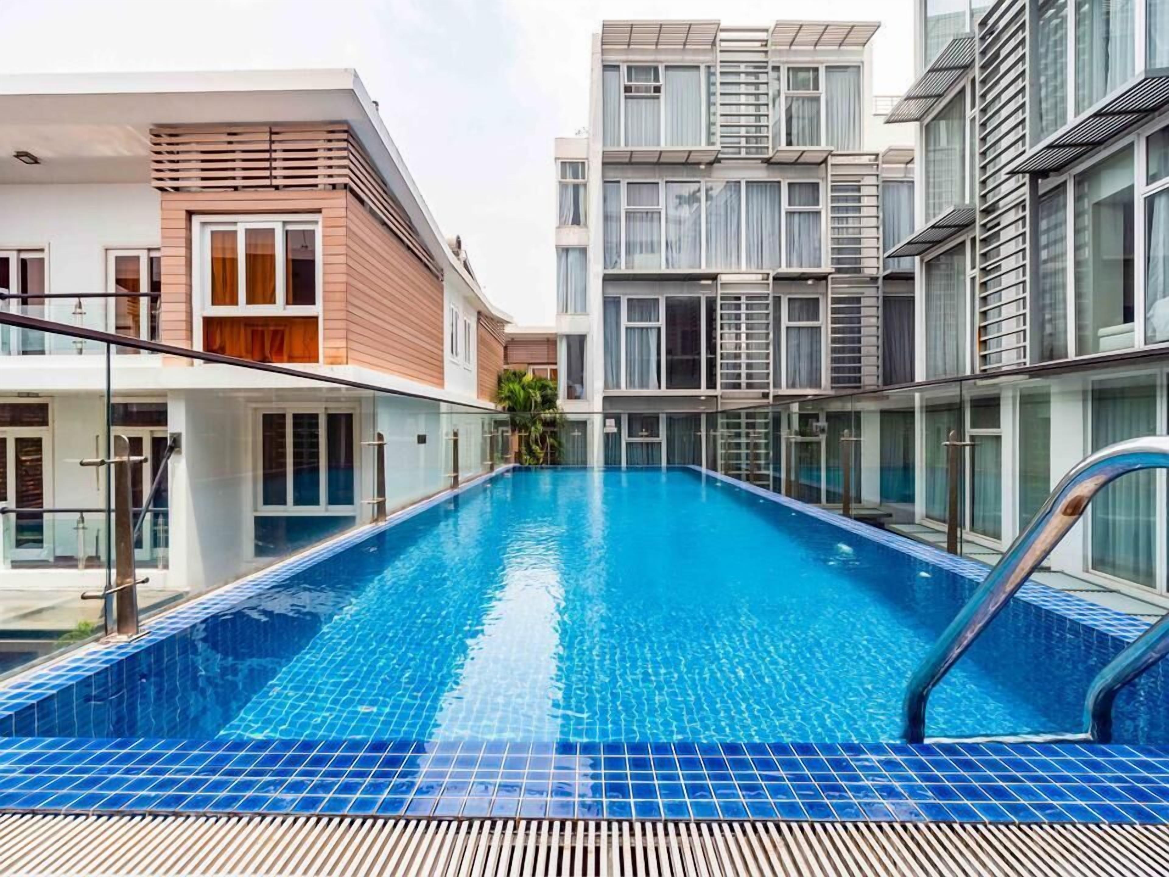 Un hotel moderno con piscina, que presenta un diseño contemporáneo con barandillas de vidrio y un deck con baldosas.