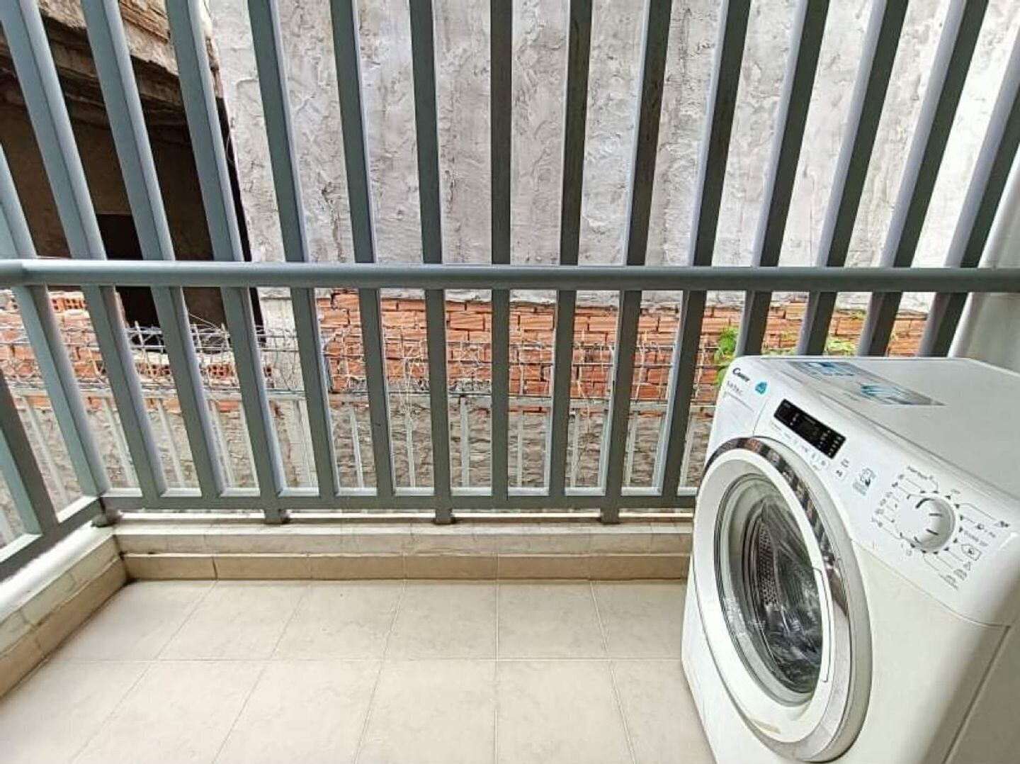 Un espace dédié à la lessive, comprenant un lave-linge, une rambarde en métal et donnant sur un mur de briques.