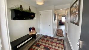 A hallway with a bench, a rug, a wall-mounted shelf with plants, and a door leading to another room. - Edgewater #2 Sparrow (Polson)