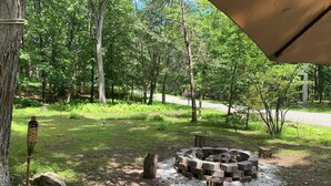 A forested campsite with a circular fire pit surrounded by logs, a wooden post, and a rock. -  EL EDEN PLACE TO REST AND ENJOY (EL EDEN LUGAR PARA DESCANSAR Y DISFRUTAR  (Bushkill)