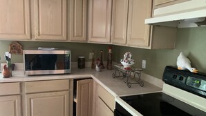 A kitchen with wooden cabinets, a stainless steel microwave, a black stove, and a small decorative table. -  EL EDEN PLACE TO REST AND ENJOY (EL EDEN LUGAR PARA DESCANSAR Y DISFRUTAR  (Bushkill)