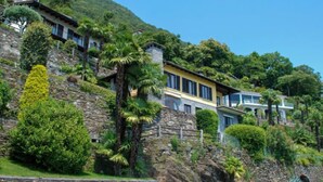 Um terreno em encosta com vários edifícios, vegetação exuberante e um muro de suporte de pedra.