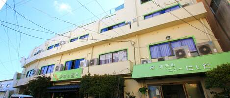 A multi-story building with a green awning, air conditioning units, and potted plants.