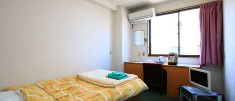 Una habitación pequeña y sencilla con cama, escritorio, televisor y ventana con cortinas.