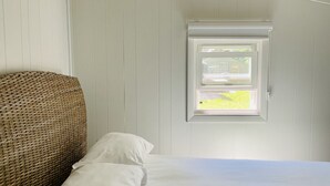 Une chambre à coucher avec un lit, du linge de lit blanc, une tête de lit en osier et une fenêtre donnant sur un paysage verdoyant.