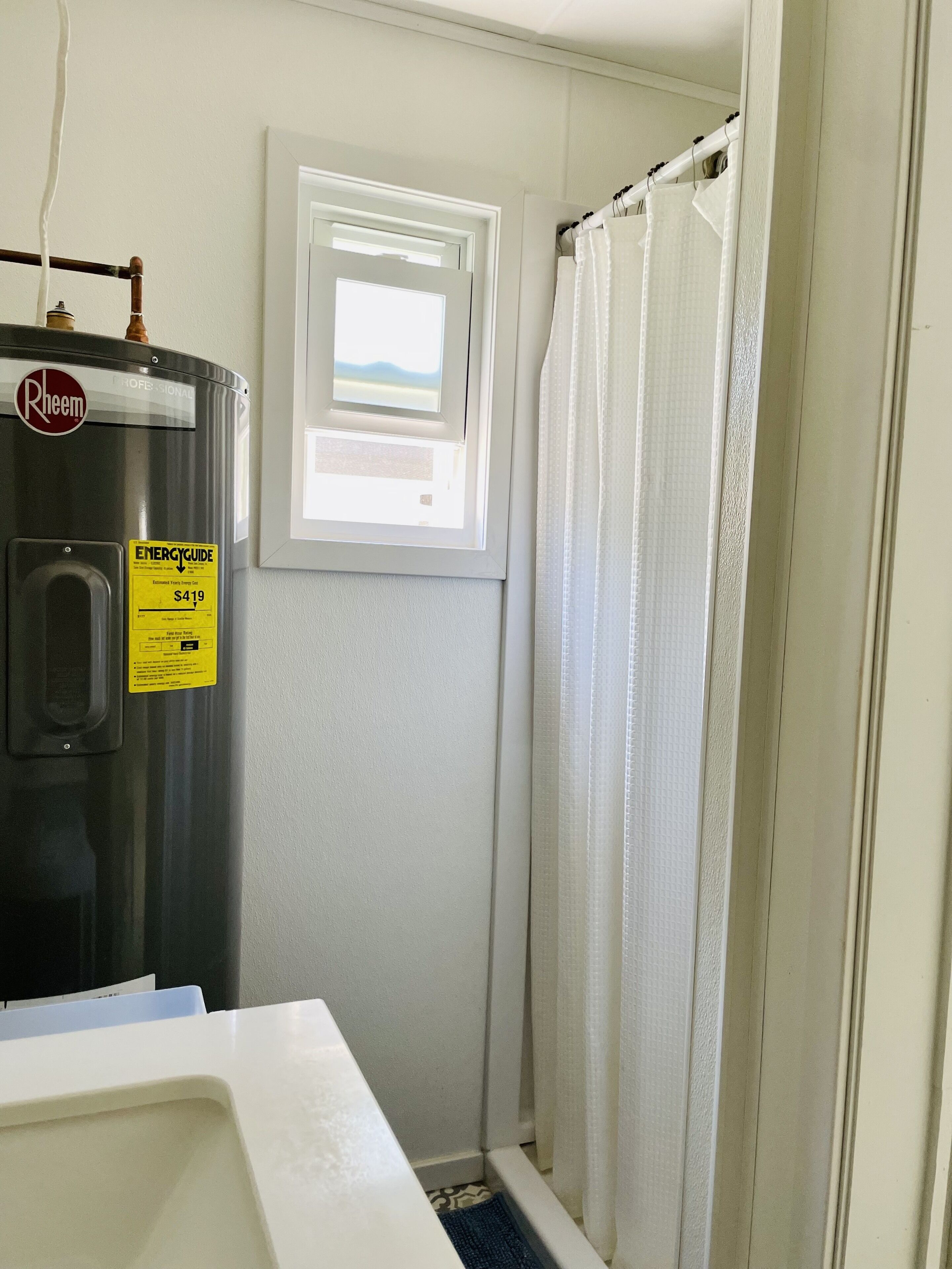 Un baño con calentador de agua, ventana y cortina de ducha.