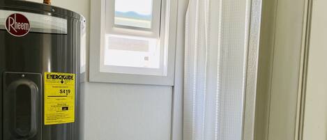 Un baño con calentador de agua, ventana y cortina de ducha.