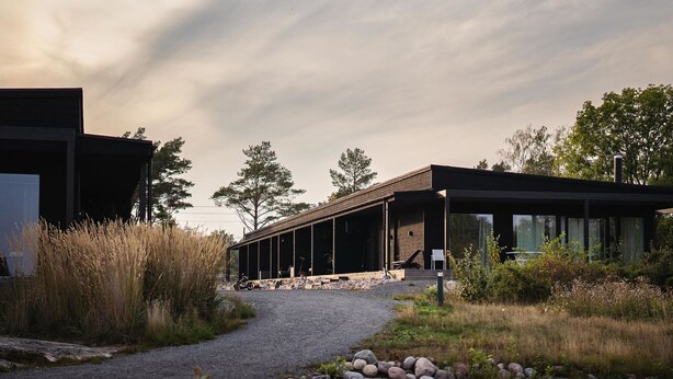 A modern building with a covered outdoor area, a gravel path, and surrounding natural vegetation.