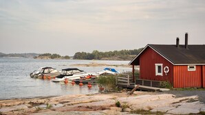 A red wooden cabin by a lake with boats docked nearby.