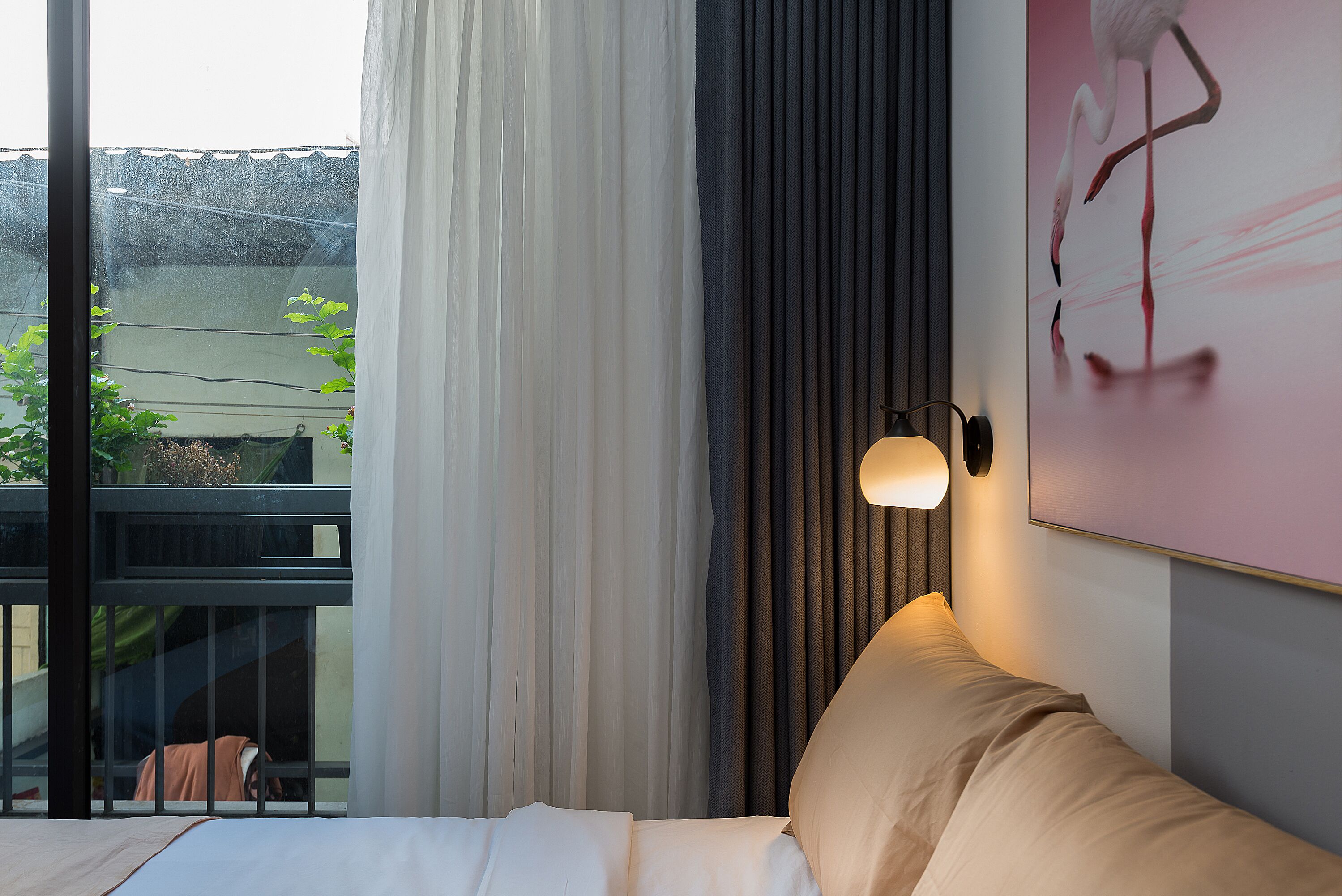 A modern bedroom with a large window, a bed, a wall-mounted light, and a painting.