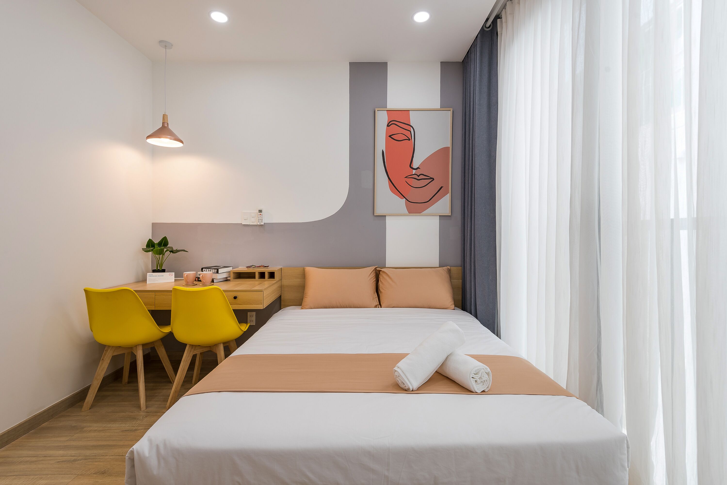 A hotel room with a bed, a desk with chairs, a painting on the wall, and a window with curtains.