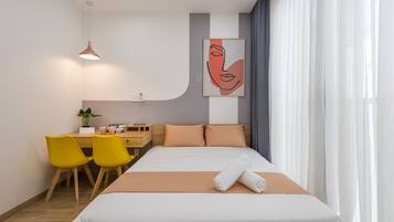 A hotel room with a bed, a desk with chairs, a painting on the wall, and a window with curtains.