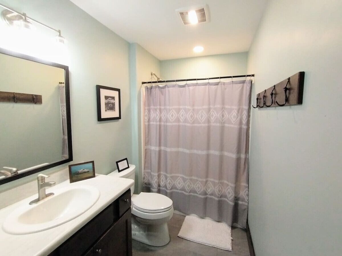 A bathroom with a white sink, a toilet, a shower curtain, and a towel on the floor.