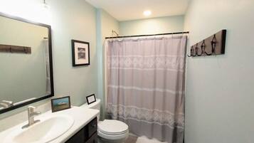 A bathroom with a white sink, a toilet, a shower curtain, and a towel on the floor.