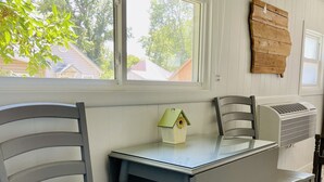 Un comedor con mesa y sillas, una ventana con vista a casas y un aire acondicionado instalado en la pared.