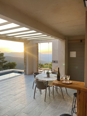 Eine Terrasse mit Pool, Esstisch, Stühlen und einer Weinflasche.
