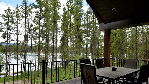 A wooden deck with a table and chairs overlooking a lake, surrounded by trees. - Waterfront Redtail Retreat Lodge in Silverhawk Subdivision, Island Park Idaho (Island Park)