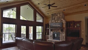 A spacious living room with a stone fireplace, leather seating, and large windows. - Waterfront Redtail Retreat Lodge in Silverhawk Subdivision, Island Park Idaho (Island Park)