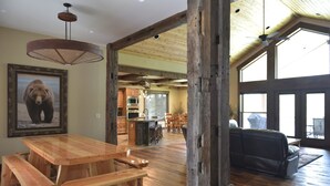 A spacious living area with a wooden dining table and benches, a large bear painting on the wall, and a view of the kitchen and dining area through an open doorway. - Waterfront Redtail Retreat Lodge in Silverhawk Subdivision, Island Park Idaho (Island Park)
