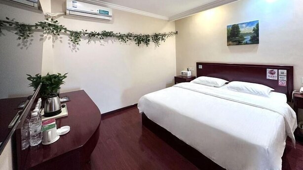 A hotel room with a bed, a bedside table with a lamp, a wall-mounted air conditioner, and a small painting. - Greentree Inn Linyi Yitang Town Shuangling Road Ex (Linyi)