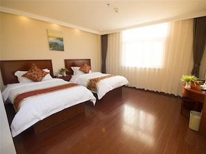 Habitación de hotel con dos camas, un cuadro en la pared, un ventanal con cortinas y una mesita con una planta.